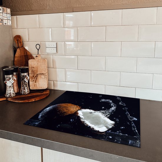 Een kokosnoot met waterplassen op een inductiebeschermer, geplaatst op een kookplaat met witte tegels erachter.
