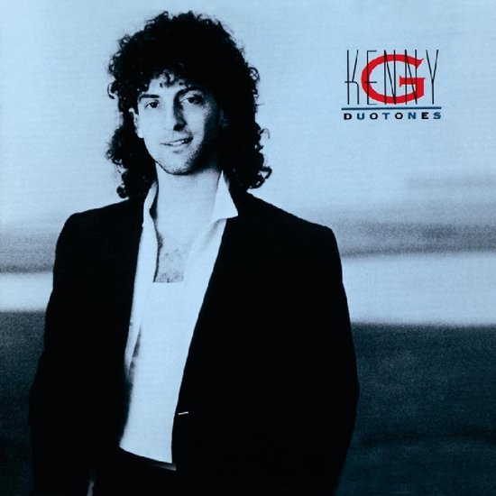 Kenny G, staand, met krullend haar, gekleed in een zwart jasje, wit overhemd en wit T-shirt.