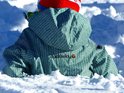 Kind in groen regenpak met visgraatpatroon zit in de sneeuw.