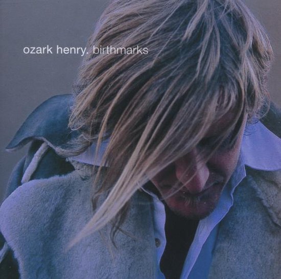 Ozark Henry's album "Birthmarks" met een close-up van een man met lang blond haar en een grijze jas.