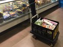 In een supermarkt duwt iemand een Stanley steekwagen met twee gevulde zwarte kratten.
