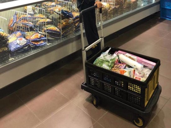 In een supermarkt duwt iemand een Stanley steekwagen met twee gevulde zwarte kratten.
