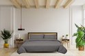 Un lit double avec une housse de couette gris foncé et deux taies d'oreiller, fait dans une chambre lumineuse avec des plantes.
