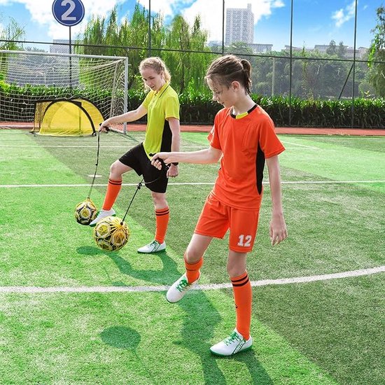 Twee meisjes in sportkleding trainen met voetbal aan elastiek op veld.