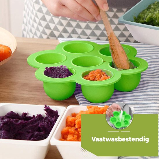 Groene siliconen bakjes in bloemvorm, gevuld met paarse puree en oranje worteltjes. Een hand voegt eten toe met een houten lepel.
