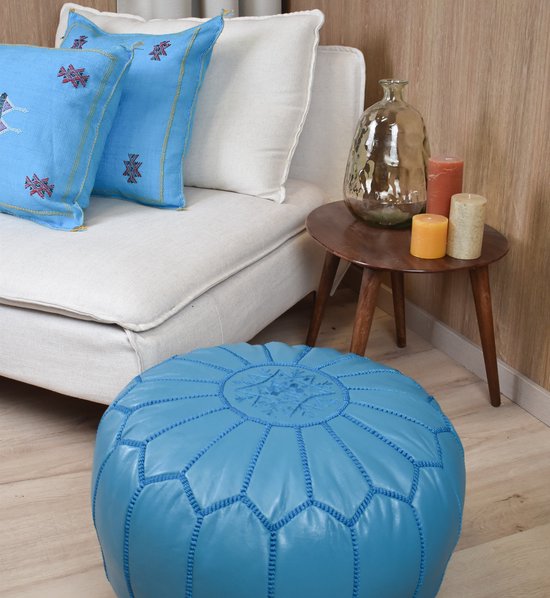 Turkooizen poef met geborduurd stermotief, naast een witte bank met turquoise kussens.