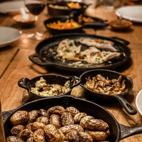 Een tafel vol met diverse gerechten in gietijzeren pannen: aardappelen, vis, en groenten.
