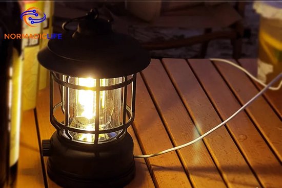 Lanterne de camping noire allumée sur une table en bois avec un câble blanc.
