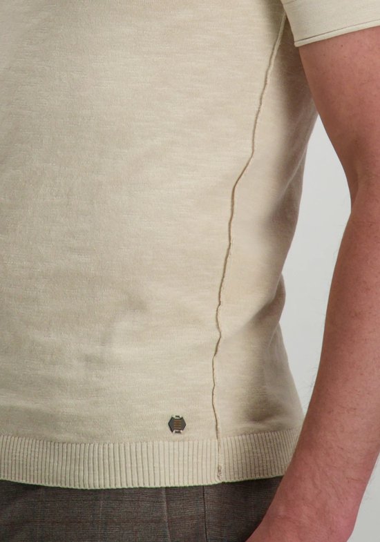 Vue de côté d'un haut beige avec une couture contrastante et un logo.