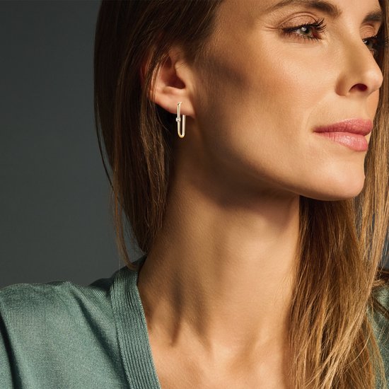Model met gouden oorbellen met zirkonia, in de vorm van een paperclip.
