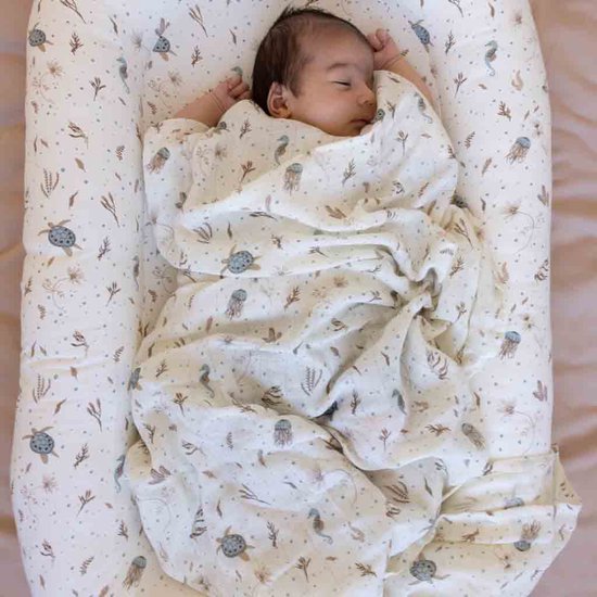 Baby ingewikkeld in een crème hydrofiele doek met zeedessins, liggend in een nestje.