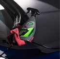 Flacon pulvérisateur gris avec accents verts et noirs, sur le capot d'une voiture foncée, avec un chiffon rouge à côté.