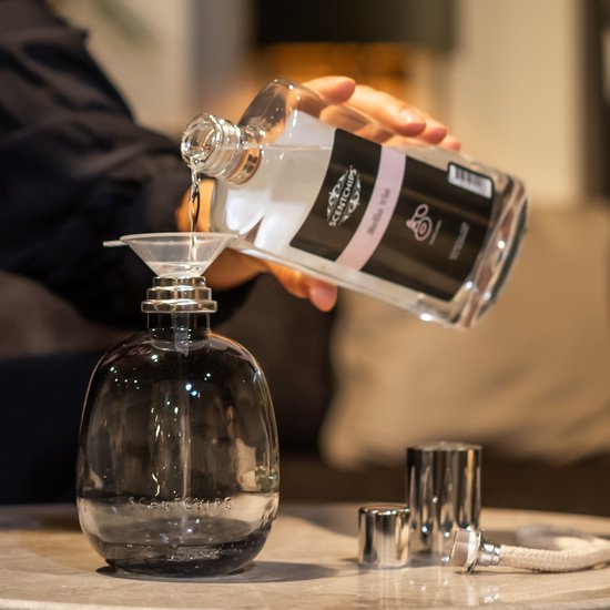 Handen vullen een glazen geurbrander met geurolie uit een fles met trechter.