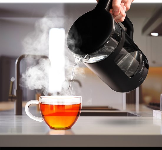 Een zwarte FAWLR waterkoker met een glazen kan, schenkt kokend water in een doorzichtige mok gevuld met thee.