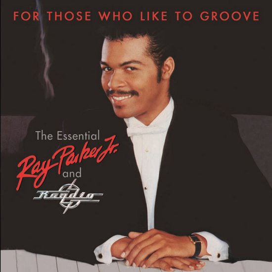Ray Parker Jr. in zwart pak met witte strik, kijkt over zijn schouder met een glimlach.