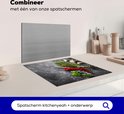Inductiebeschermer met betonprint, naast een zilveren spatbord, in een keukenopstelling.