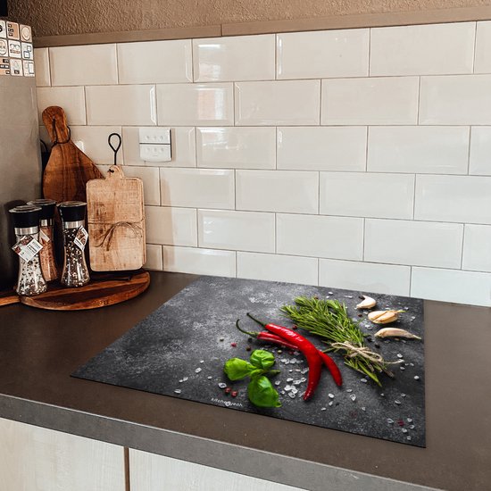 Inductiebeschermer met betonprint, met rode pepers, knoflook en kruiden, geplaatst op een keukenaanrecht.