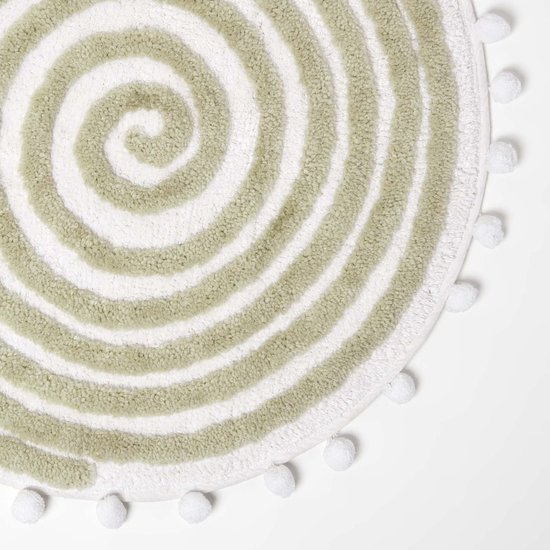 Close-up van de ronde, saliegroene badmat met spiraalpatroon en witte pompons.