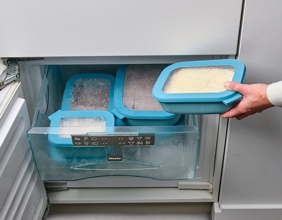Main retire un récipient bleu avec une couche de riz d'un tiroir de congélateur couvert de givre.