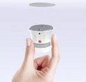 Hand toont rookmelder met twee magneten, zilverkleurige schijf zweeft erboven.