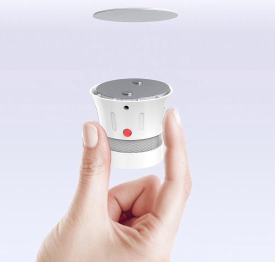 Hand toont rookmelder met twee magneten, zilverkleurige schijf zweeft erboven.