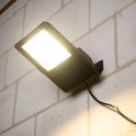 Warme gloed van verlichte zwarte LED-schijnwerper op een bakstenen muur.