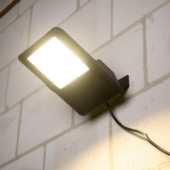 Warme gloed van verlichte zwarte LED-schijnwerper op een bakstenen muur.
