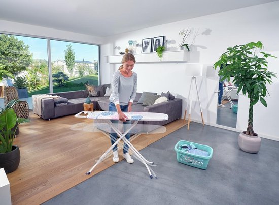 Vrouw vouwt strijkplank met bloemenprint (roze, blauw, wit).