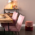 Tweekleurige poef met roze en bordeaux rode stoffen zittingen, gescheiden door een gouden ring, staat naast een eettafel met roze stoelen.
