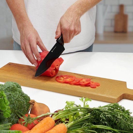 Persoon snijdt rode paprika met zwart keukenmes, groenten op tafel