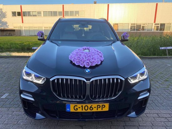 Vooraanzicht van zwarte BMW met paarse bloemen op de motorkap.