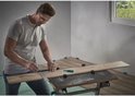 Een man in een grijs T-shirt gebruikt een wolfcraft winkelhaak en markeert een houten vloerplank.