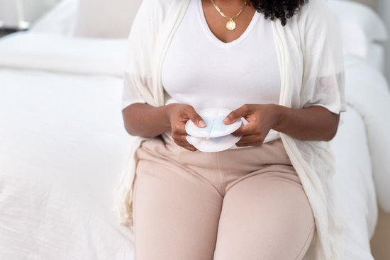 Vrouw in witte top en beige broek die twee zoogcompressen vasthoudt.