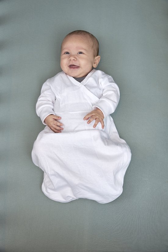 Een lachende baby in een wit kruippakje, liggend op een groen textiel.