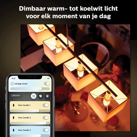 Een smartphone met de Philips Hue app toont "Living room" en bedieningsknoppen voor lampen, met op de achtergrond een lamp met vier hangende kaarslampen die warm wit licht geven.