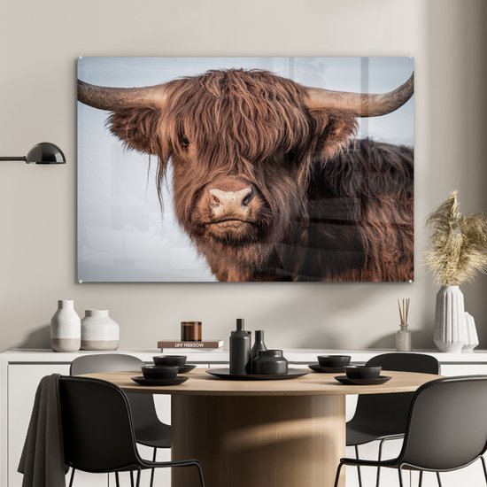 Glasafbeelding van een bruine Schotse hooglander met grote hoorns, hangend boven een eettafel.