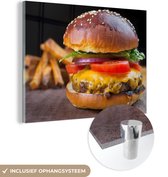 MuchoWow® Glasschilderij 120x90 cm - Schilderij acrylglas - Hamburger met frietjes op de achtergrond - Foto op glas - Schilderijen
