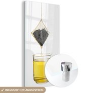 MuchoWow® Glasschilderij 20x40 cm - Schilderij acrylglas - Een theezakje laat water druppen in de theebeker - Foto op glas - Schilderijen