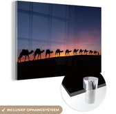 MuchoWow® Glasschilderij 60x40 cm - Schilderij acrylglas - Silhouet van een karavaan met kamelen tegen een zonsondergang in de Sahara wWestijn - Foto op glas - Schilderijen