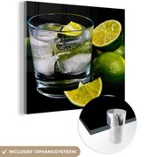 MuchoWow® Glasschilderij 90x90 cm - Schilderij acrylglas - Glas gin en tonic op ijs omgeven door limoenen - Foto op glas - Schilderijen
