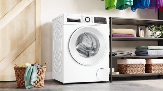 Witte Bosch wasmachine met open deur, gevuld met schone was, naast een mand met wasgoed.