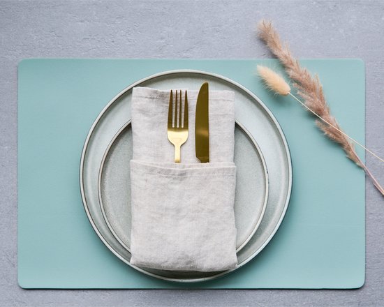 Een mintgroene placemat met een bord, servet en gouden bestek.