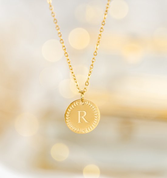 Gouden ketting met een rond medaillon met de letter R, omringd door een lauwerkrans.