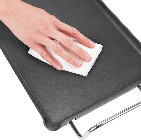 Hand veegt met een wit doekje over een zwarte elektrische bakplaat.