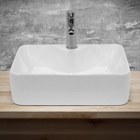 Lavabo rectangulaire en céramique blanche avec robinet chromé sur un support en bois.