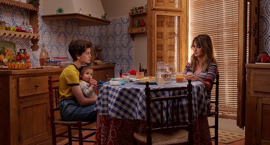 Twee vrouwen en een baby aan een tafel met blauw-wit geblokt tafelkleed. Vrouw met bruin haar draagt gestreept shirt.
