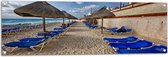 WallClassics - Tuinposter – Blauwe Ligbedden op Strand met Rieten Parasols - 120x40 cm Foto op Tuinposter (wanddecoratie voor buiten en binnen)