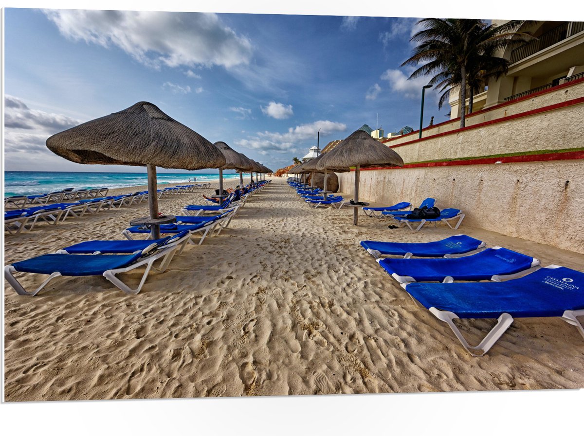 PVC Schuimplaat- Blauwe Ligbedden op Strand met Rieten Parasols - 105x70 cm Foto op PVC Schuimplaat