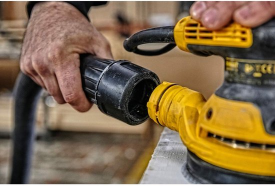 Handen koppelen de stofzuigerslang aan de gele DeWalt schuurmachine.
