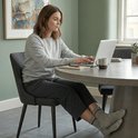 Vrouw met een grijze trui en broek, zittend aan een tafel met een laptop, draagt lichtgrijze sokken.